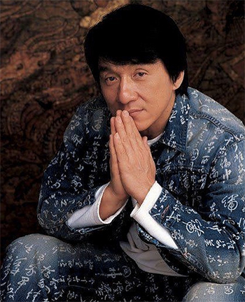 Jackie Chan seated, hands folded, in a jean outfit patterned with Chinese calligraphy